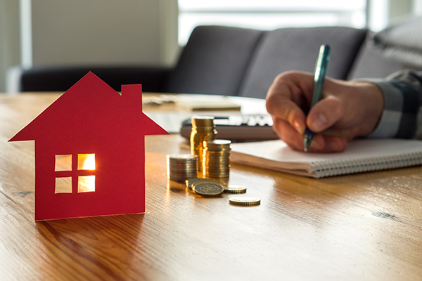 An image of a man working out finances with a cardboard illustration of a house in the foreground.